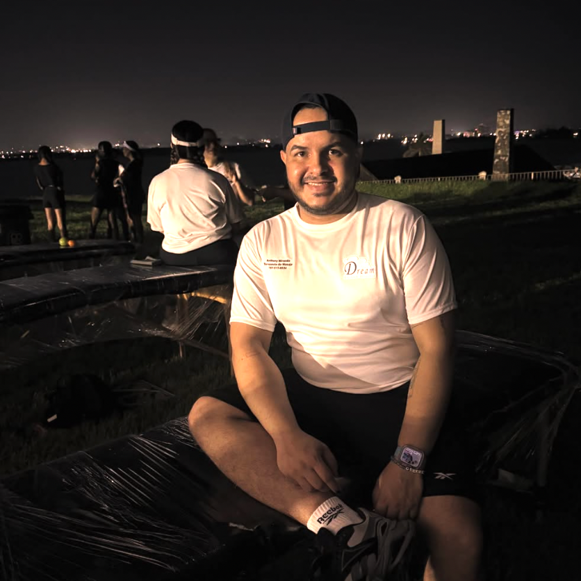 Man sitting on a car at night with city lights in the background
