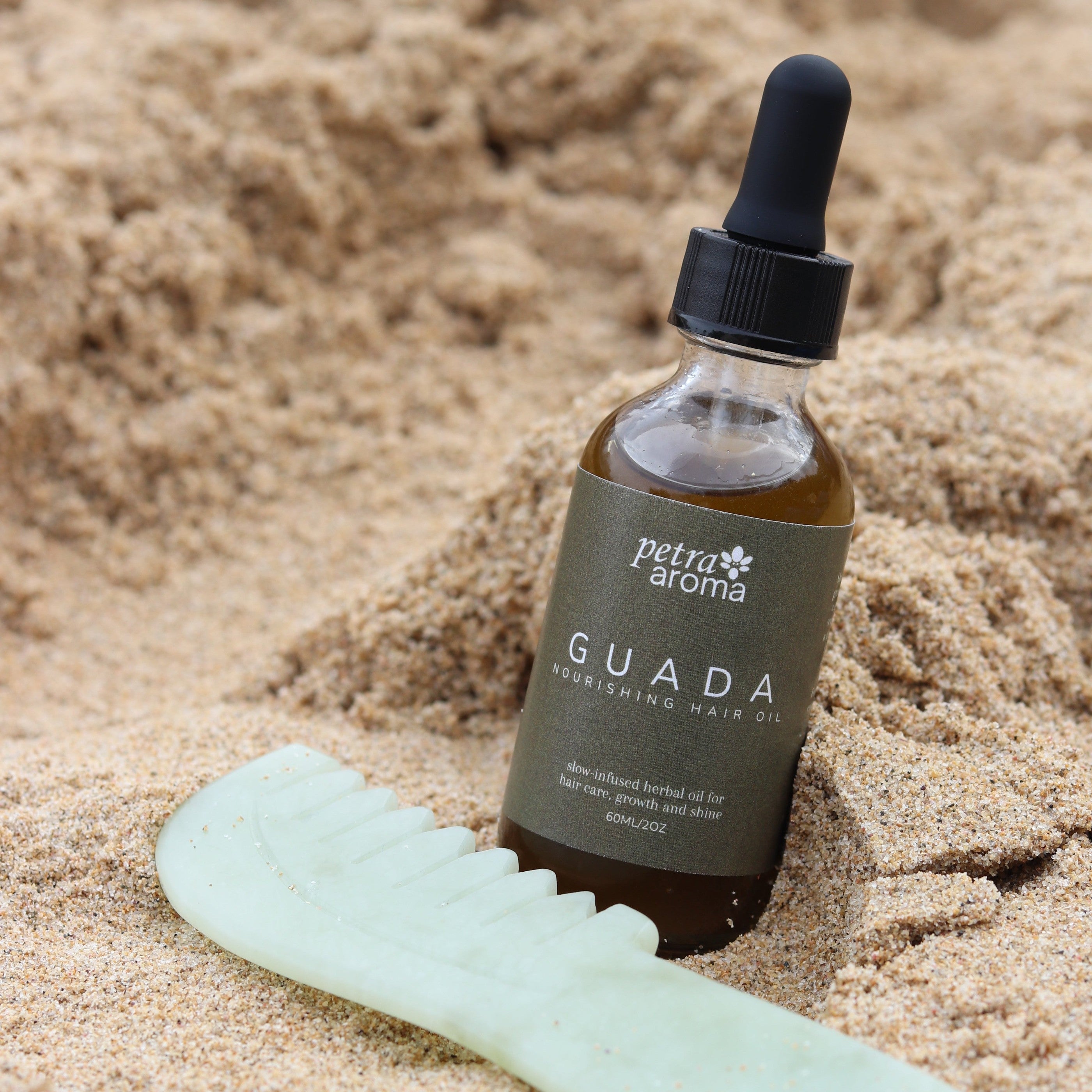 Guada hair oil and jade scalp comb in beach sand